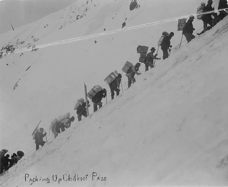 約1898年，淘金者攜帶物資攀越 Chilkoot Pass；許多人必須來回搬運，才能湊足進入內陸所需的裝備