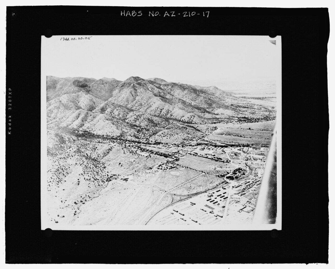 AERIAL PHOTOGRAPH TAKEN IN 1944, LOOKING TO THE WEST. THE 1916 STABLES ARE VISIBLE TO THE EAST OF THE FOOTHILLS OF THE HUACHUCA MOUNTAINS (FORT HUACHUCA HISTORICAL MUSEUM, PHOTOGRAPH HABS AZ-210-17.tif